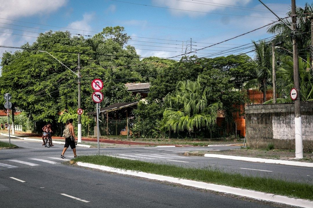 Pedestrian crossing a leafy suburban street beside a cyclist