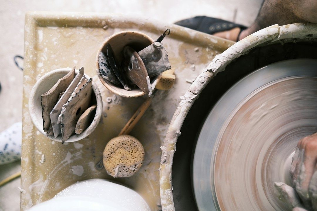 Potter’s hands shape clay on a spinning wheel beside tools