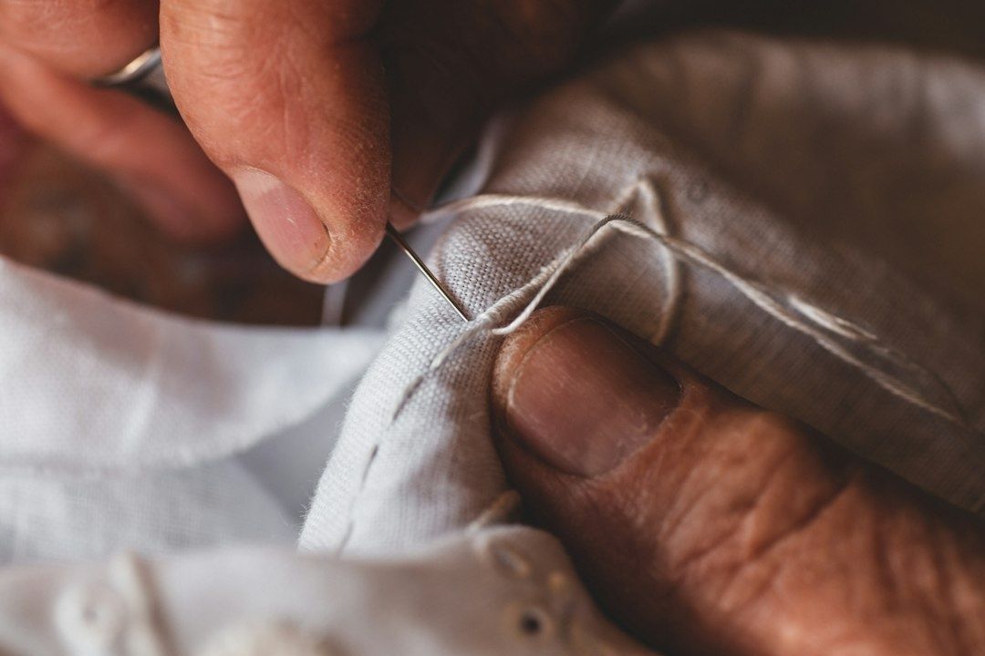 Close-up of hands sewing a needle through folded linen fabric
